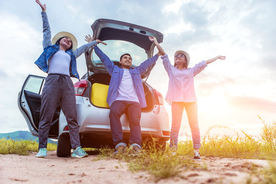 Happy Young Asian Friend Sitting And Standing Behind The Car On Vacation Holiday With Travel Road Trip. Car Travel Concept.