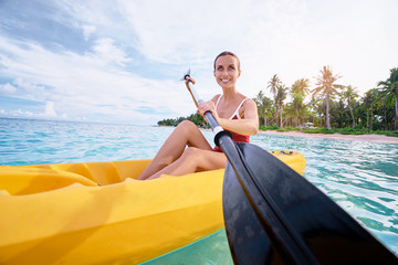 Active vacation. Young woman paddling the sea kayak near tropical bay.