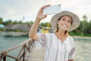 Vacation and technology. Young woman taking selfie with her  smartphone on tropical beach. Focus on cellphone.