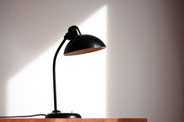 an antique black table lamp from the 20s bauhaus era standing on an old desk commode isolated on white background very rare in original condition design icon close up living room minimalistic design