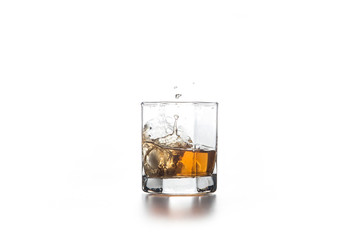 Whiskey splash from the fallen ice cube into glass with beverage on light background..