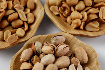 wood plates of salted peanuts and pistachios on white background. snack to beer