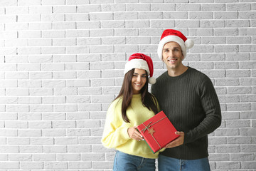 Obraz na płótnie Canvas Happy young couple with Christmas gift against brick wall