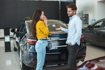 beautiful young couple man and woman deciding which car to choose in dealership center