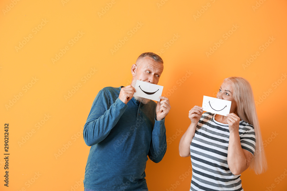 Poster Mature couple holding paper sheets with drawn smiles against color background