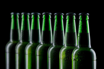 Row of wet glass bottles of beer on dark background