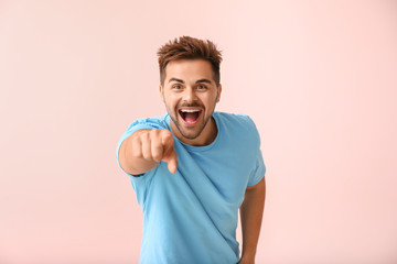 Portrait of happy young man pointing at viewer on color background