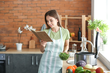 Woman with recipe book and modern multi cooker in kitchen