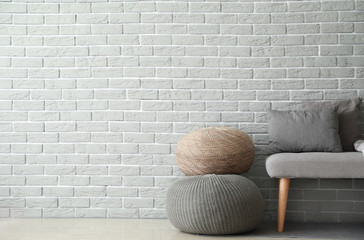 Cozy sofa with poufs near brick wall in room