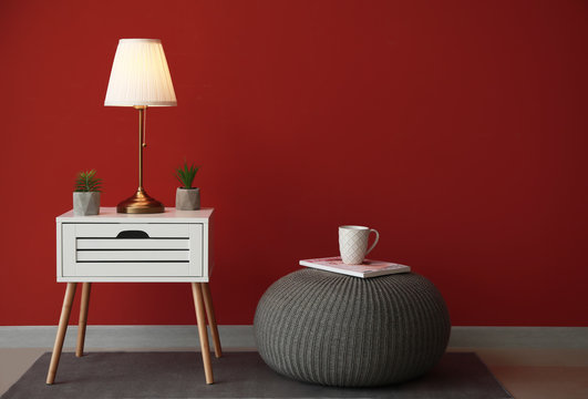 Modern table with lamp and pouf near color wall in room