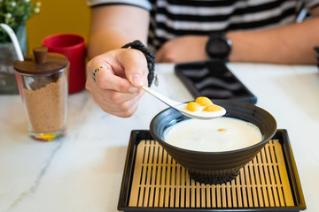 Close up hand of people using spoon to holding ginkgo with coconut milk on black bowl in cafe ,Dessert of thailand.