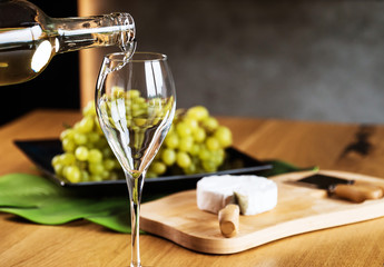 Pouring White wine with branches of grapes on a wooden table.