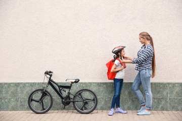 Mother helping her daughter to put on bicycle helmet outdoors