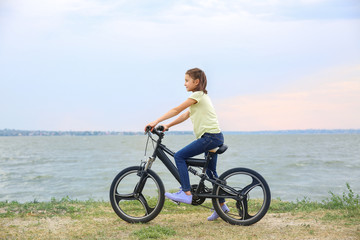 Obraz premium Little girl riding bicycle near river