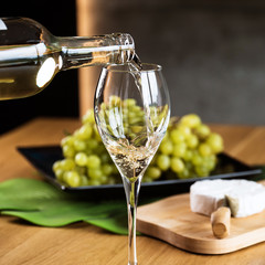 Pouring White wine with branches of grapes on a wooden table.