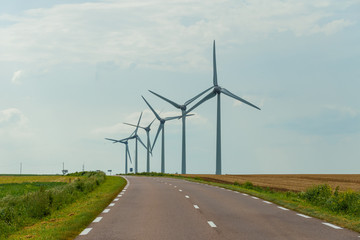 Wind turbines of a power plant for electricity generation close to country road in Normandy, France. Countryside landscape. Environmentally friendly electricity production