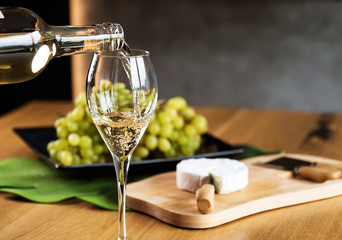 Pouring White wine with branches of grapes on a wooden table.