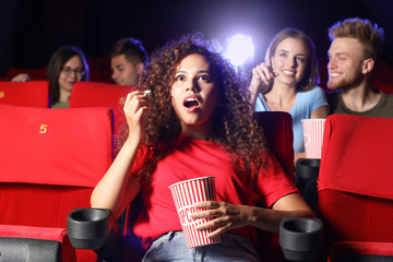 African-American woman with popcorn watching movie in cinema