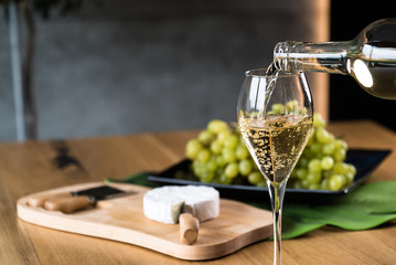 Pouring White wine with branches of grapes on a wooden table.