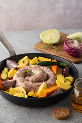 Raw sausages with potatoes, zucchini, carrots and thyme in a grill pan.