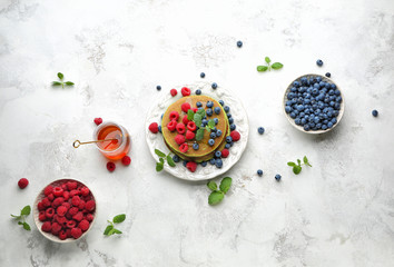 Plate with green pancakes, fresh berries and honey on light background