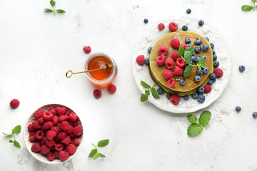Plate with green pancakes, fresh berries and honey on light background