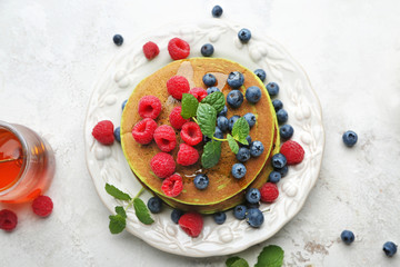 Plate with green pancakes, fresh berries and honey on light background