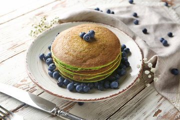 Plate with green pancakes and fresh berries on white table