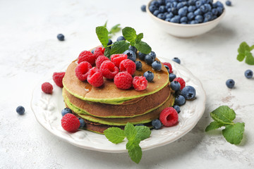 Plate with green pancakes and fresh berries on light background