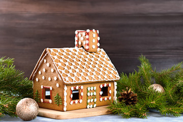 Decorated gingerbread house closeup with pine decorations and golden balls in background.