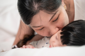 Obraz na płótnie Canvas Asian mother kissing and touching a baby that sleeping on bed with gently and love, feeling happy. mother and baby concept.