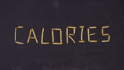 Word CALORIES laid out of long sticks of fried french fries on black background.