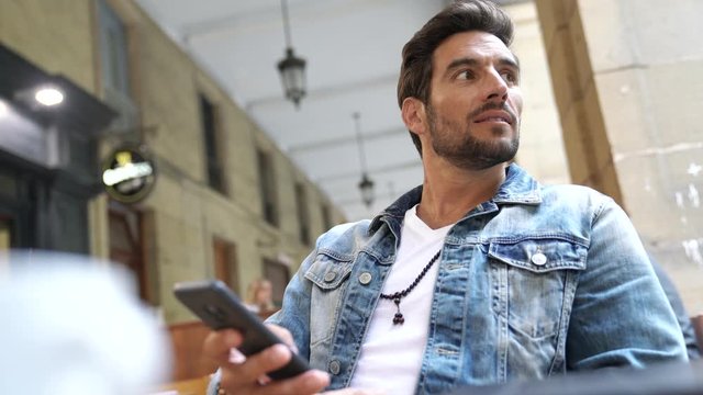 Trendy guy connected on smartphone at coffee shop