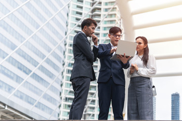 group of asian business people working and discussing something positive with his mature colleague and using a laptop at outdoor in the capital