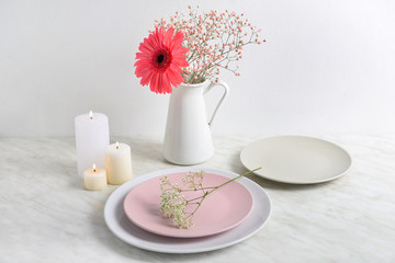 Beautiful burning candles with plates and flowers on table