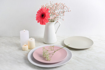Beautiful burning candles with plates and flowers on table