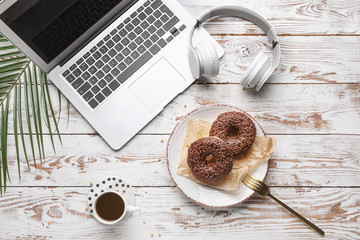 Tasty donuts with laptop, headphones and cup of coffee on white wooden table