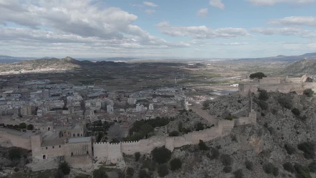 Drone dolly out an of Xativa castle during sunny summer day and blue skies with city centre and mountains in the background during travel through Spain