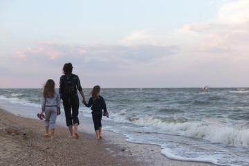 Mother with two little daughters walks along the beach at sunset