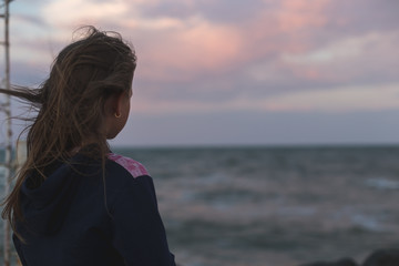 Little girl stands on the shore and looks at the sea