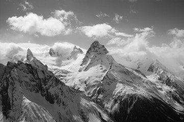 Winter snowy sunlit mountains in clouds