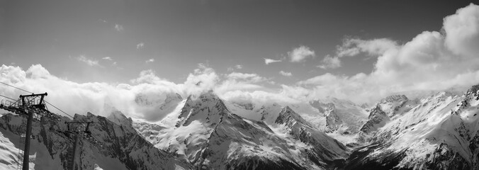 Black and white panorama of snowy sunlit mountains in clouds