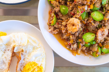 top view of traditional thai style food Spicy stir-fried shrimp with bitter or twisted cluster or stink bean ( sataw ) and shrimp paste on wooden table , Southern thai food.