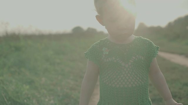Steadicam shot of a sad baby girl walking along rural field pathway on a sunny day