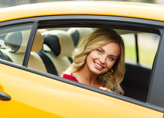 Photo of young blonde sitting in back seat of yellow taxi.