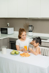 Asian children and her mom drink orange juice in the morning