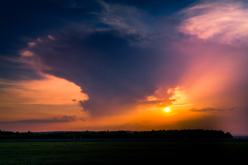 A stormy sunset with dark clouds over a rural pasture landscape.