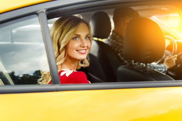 Photo of happy woman sitting in back seat of yellow taxi in summer.