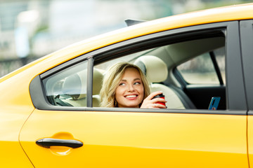 Photo of young woman with coffee in hands sitting in back seat of yellow taxi in summer on modern city background