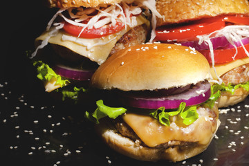 Fast food concept: fat burgers with cheese and vegetables on a dark background